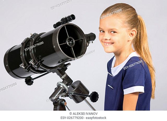The young astronomer at the telescope is smiling and looking to the frame