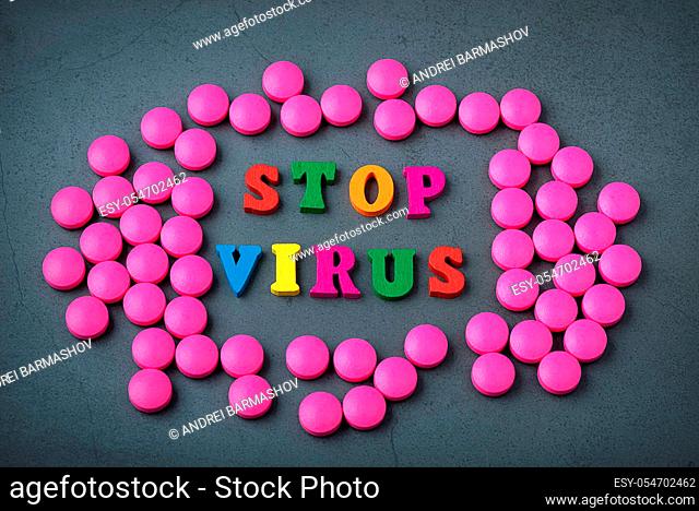 The stop sign consists of multicolored letters in a frame of bright pink pills scattered on a gray background. The concept of fighting the virus and the flu...