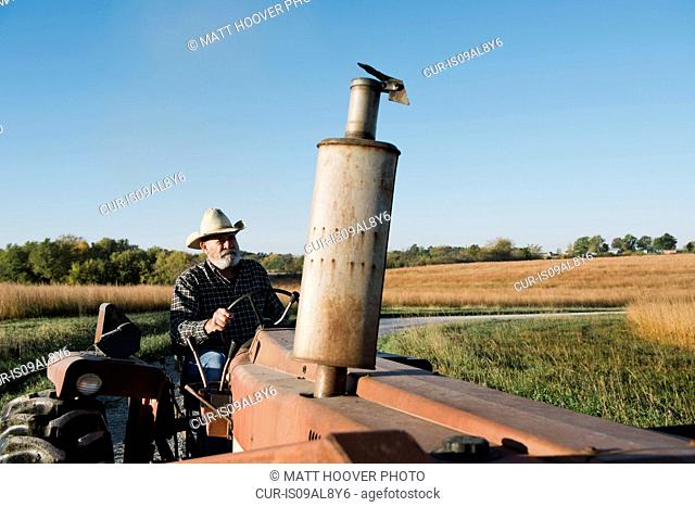 Senior male farmer driving tractor on rural road, Plattsburg, Missouri, USA
