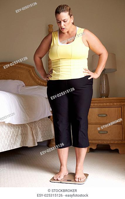 Overweight Woman Weighing Herself On Scales In Bedroom