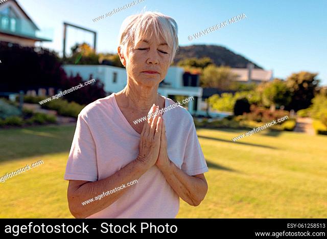 Asian senior woman with eyes closed meditating while standing on grassy land in yard, copy space