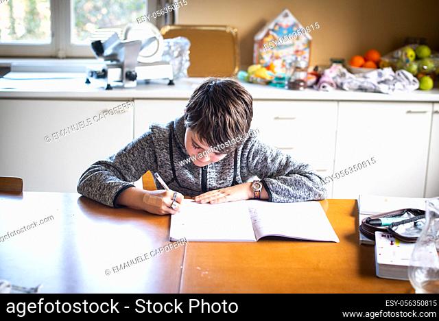 kid boy does homework on the table at home in the kitchen