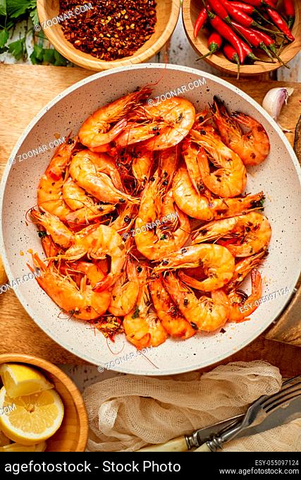Roasted Prawns on frying pan served on white wooden cutting board. Rusty wooden background. Seafood lunch or dinner concept. Top view, flat lay