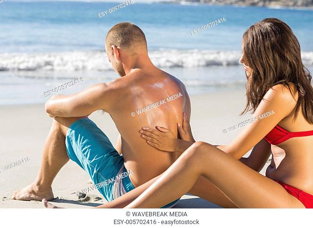 Smiling woman putting sun cream on her boyfriends back