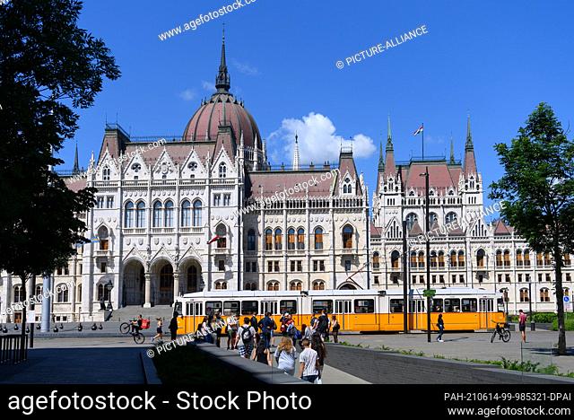 14 June 2021, Hungary, Budapest: Tourists walk out of the National Unity Monument, the Trianon Monument, while a tram runs along Lajos Kossuth Square in front...