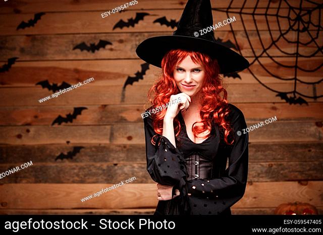 Halloween witch concept - Happy Halloween red hair Witch holding hand on her chin posing over old wooden studio background