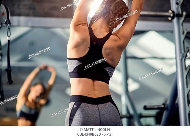 Young woman training, looking in mirror while stretching arms in gym
