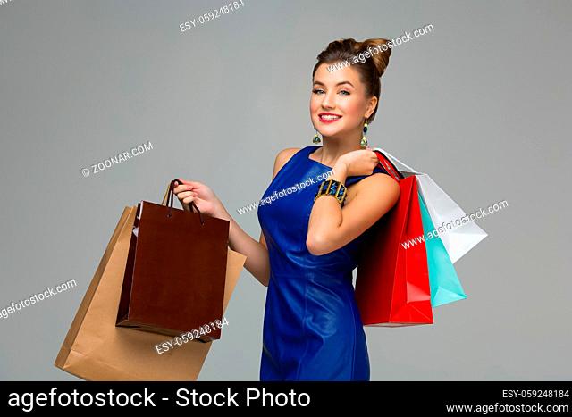 Smiling young woman in blue dress with multiple shopping bags. Happy expression. Over grey background. Copy space