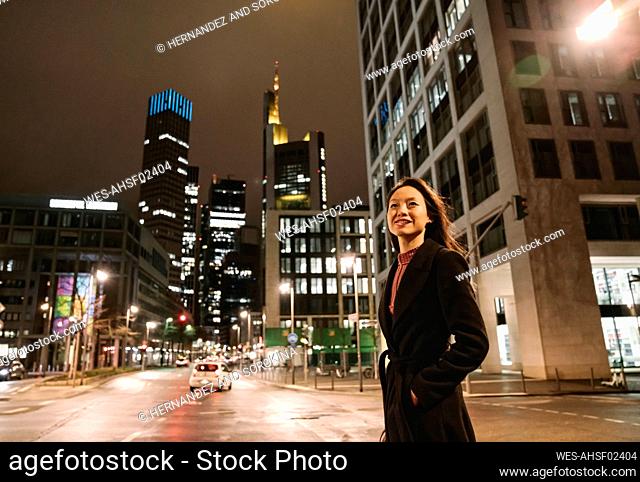 Young woman crossing the street in the city at night, Frankfurt, Germany