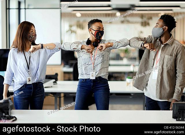 Happy business people in face masks bumping elbows in office