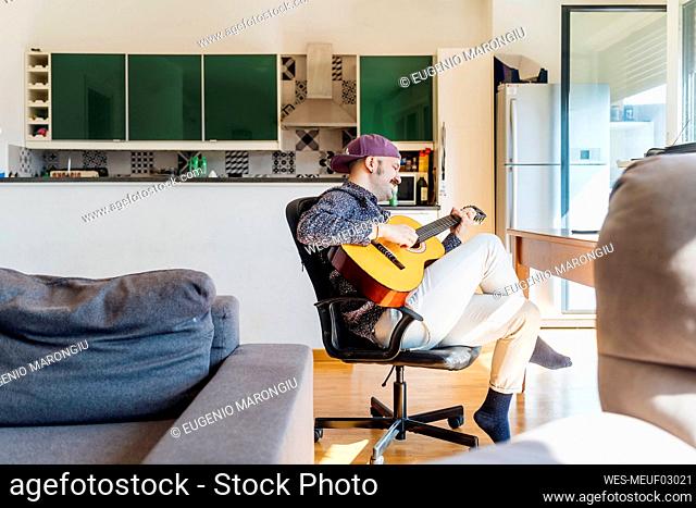 Man playing guitar on chair at home