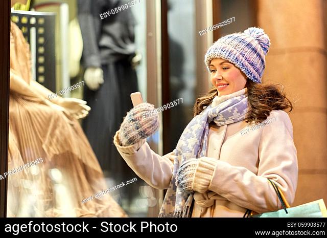 woman with shopping bags and smartphone in winter