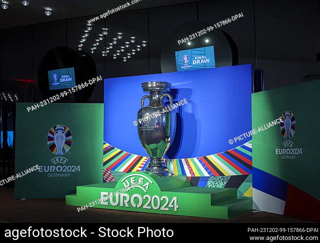 02 December 2023, Hamburg: Soccer: European Championship, draw - preliminary round in Hamburg, Elbphilharmonie. An oversized trophy on the plaza next to the red...