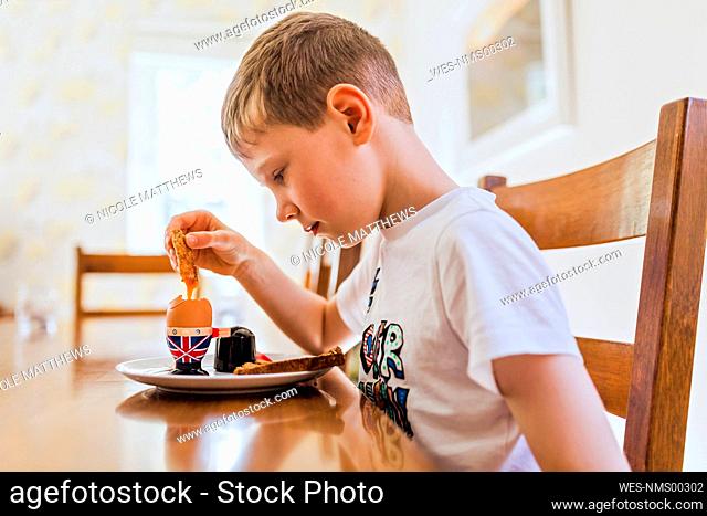 UK, sad boy sitting at breakfast table eating boiled egg