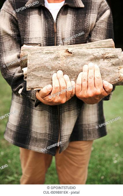 Mature man outdoors, holding firewood, mid section