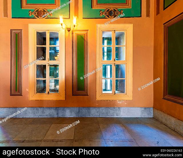 Corner orange wall with two narrow wooden window with closed green shutters, beautiful elegant rectangular green frames, and white tiled marble floor