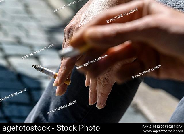 27 April 2021, Bavaria, Amberg: Smokers hold a burning cigarette in their hands. For three years, the association ""Amberger Kippenjäger"" has been campaigning...