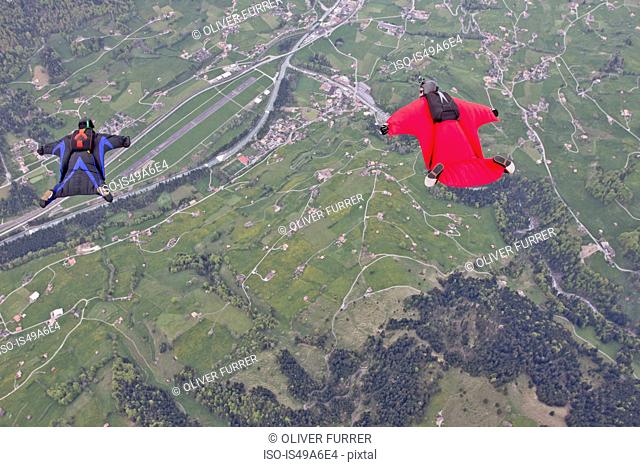 Two men flying above fields in wingsuits