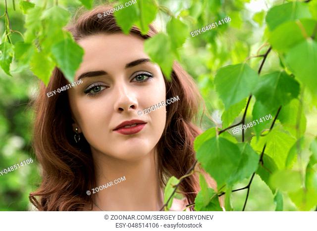 Portrait of a girl surrounded by green leaves of birch