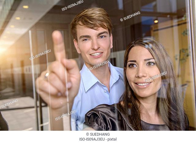 Businesswoman pointing out of glass window to colleague