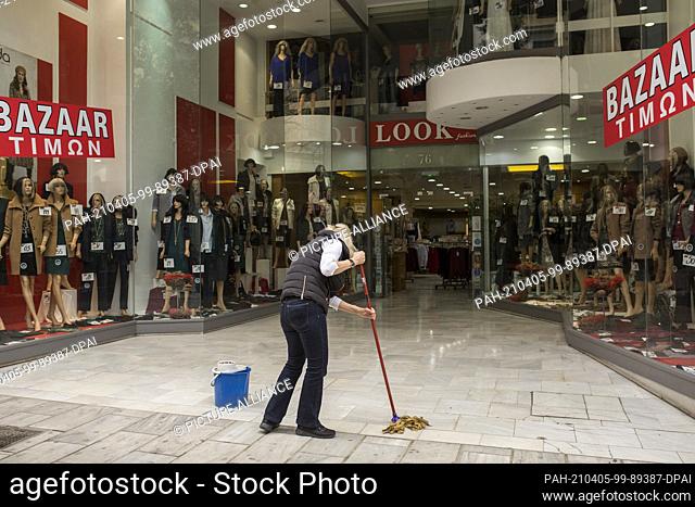 05 April 2021, Greece, Athen: A woman cleans the floor in front of a clothing store. From Monday, 05.04.2021, shops in large parts of Greece will be allowed to...