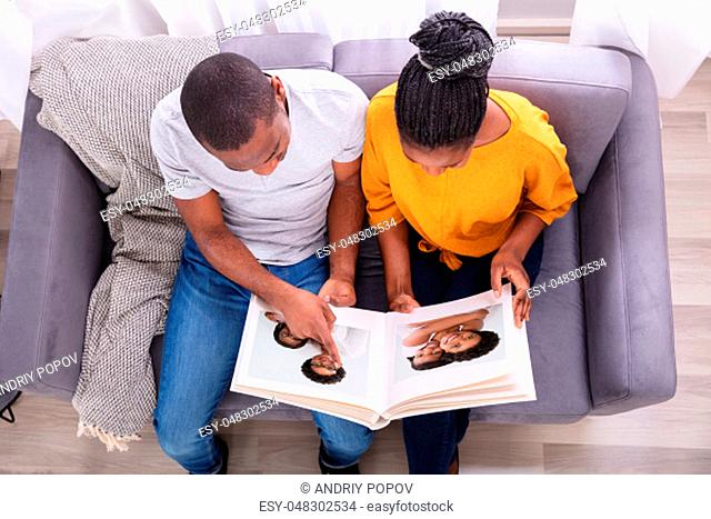 High Angle View Of An African Couple Sitting On Sofa Looking At Photo Album