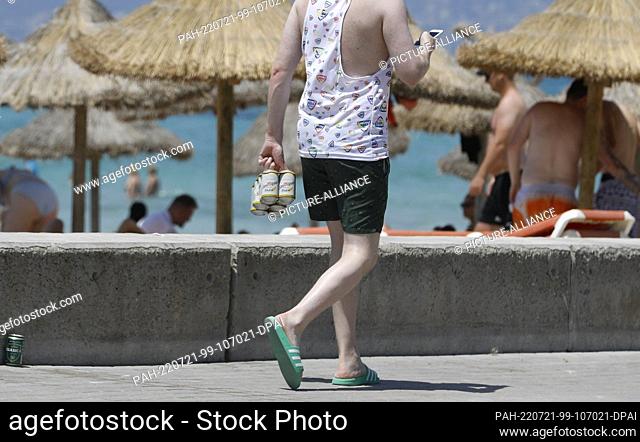 21 July 2022, Spain, Palma: A young man carries beer cans on the promenade at the beach of Arenal in Mallorca. A ""quality offensive"" was launched on Mallorca...
