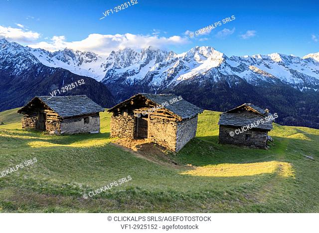 Meadows and alpine huts framed by snowy peaks at dawn Tombal Soglio Bregaglia Valley canton of Graubünden Switzerland Europe