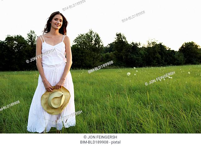 Woman standing in meadow holding straw hat