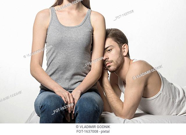 Thoughtful man leaning on girlfriend sitting at bed against white background