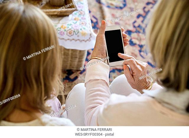 Back view of grandmother sitting beside her granddaughter using smartphone