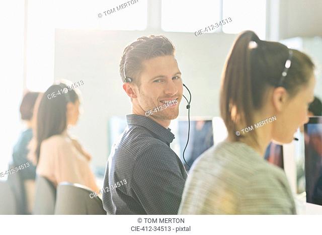 Portrait smiling male telemarketer wearing headset at computer in sunny office