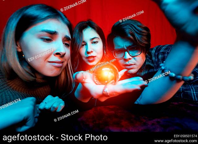 Group of people and woman fortune teller with illuminated crystal ball, close view