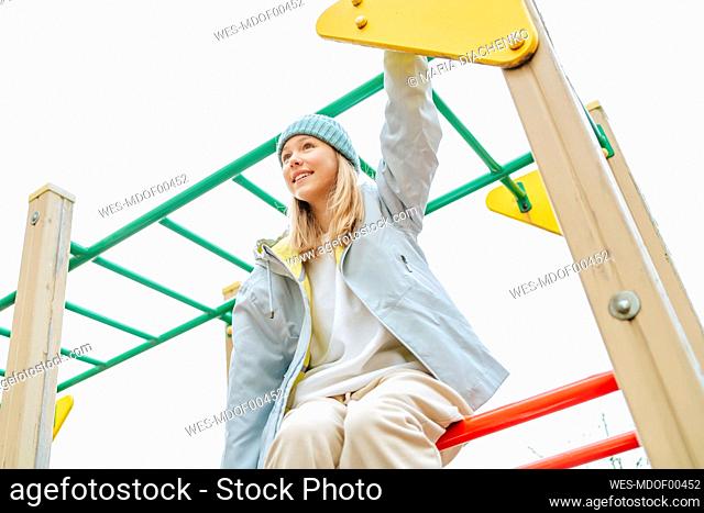 Happy teenage girl sitting on monkey bars at playground
