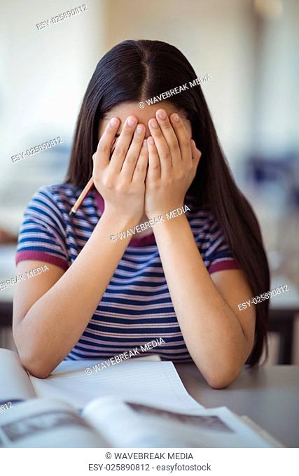Stressed schoolgirl doing covering her face in classroom