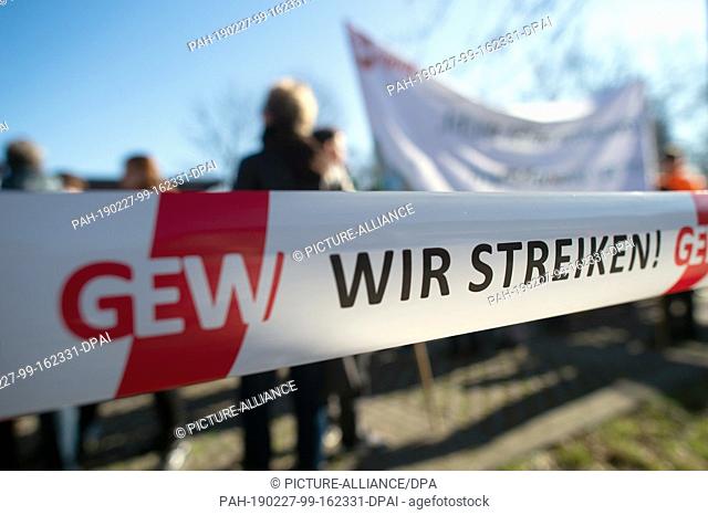 27 February 2019, Saxony-Anhalt, Magdeburg: ""We Strike"" and ""GEW"" are on two flutter ribbons behind which participants of a warning strike are standing