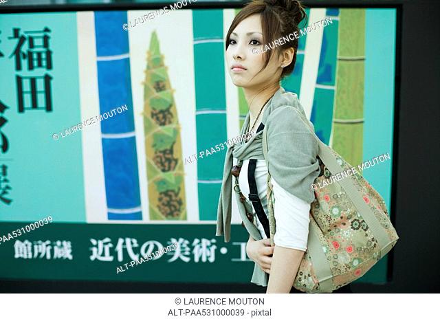 Young female walking past large poster with Japanese script, side view
