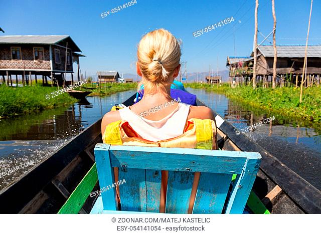Rear view of female Caucasian tourist traveling by colorful traditional wooden boat on Inle lake, Burma, Myanmar