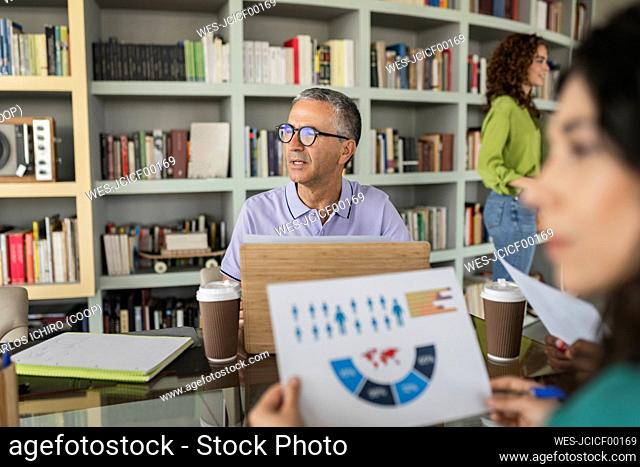 Mature businessman wearing eyeglasses sitting in front of bookshelf