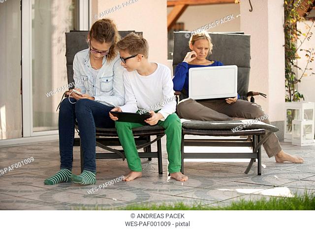 Mother and her two children relaxing with digital tablet, smartphone and laptop on the terrace