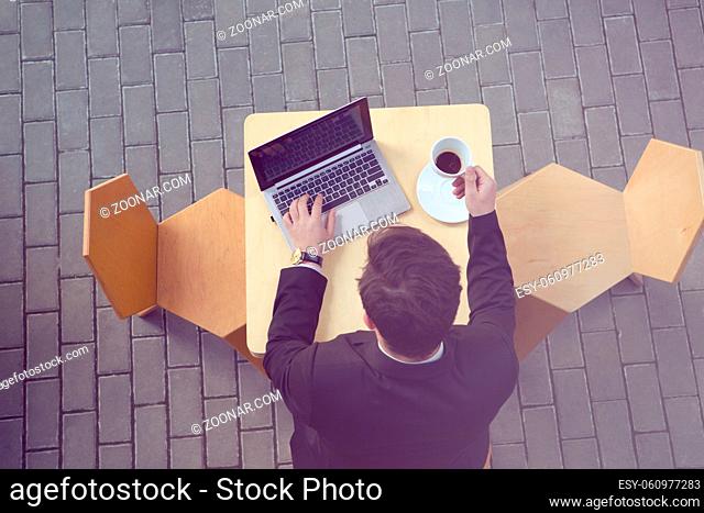 Toned top view picture of businessman using laptop computer and drinking cup of coffee in cafe or restaurant. Freelance concept