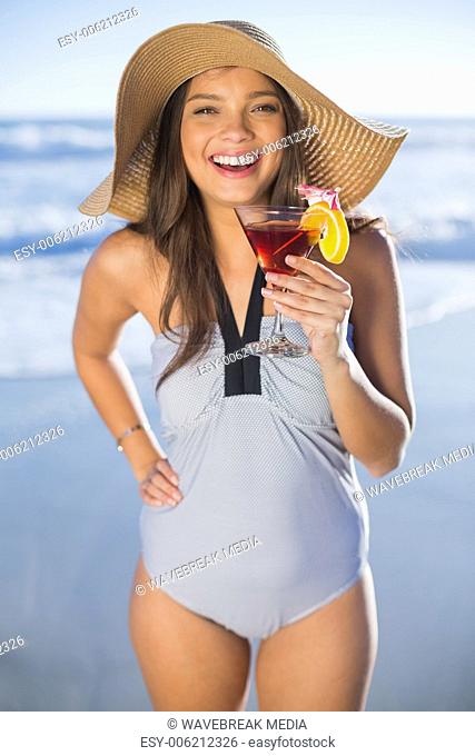 Happy woman in swimsuit wearing straw hat holding cocktail