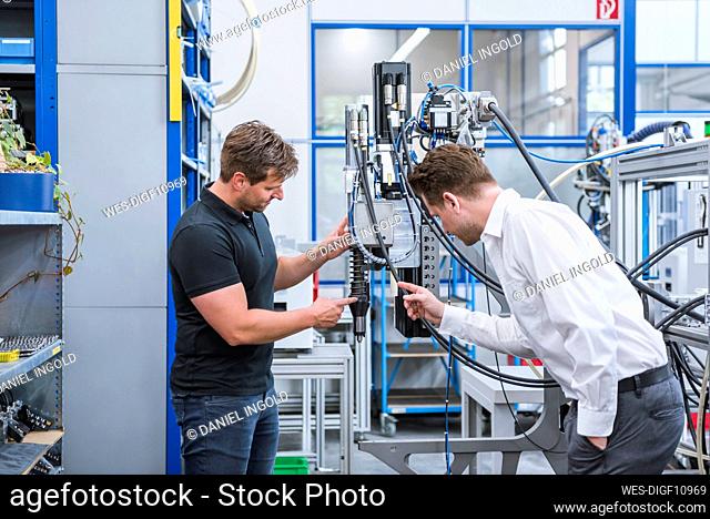 Two men having a meeting at a machine in factory