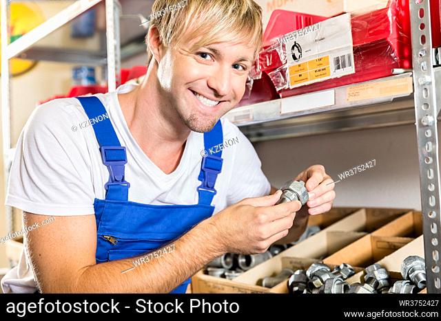 Close-up of the hands of a happy blue-collar worker holding two pipe fitting accessories in the storehouse of a modern sanitary ware shop