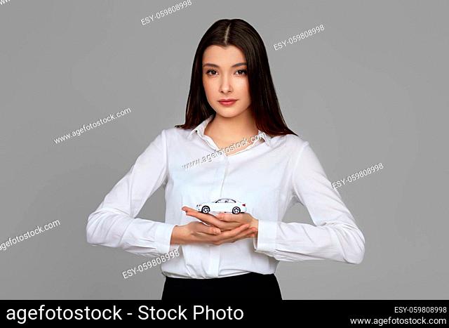 beautiful woman in shirt holding little white car on gray background. car protective and insurance
