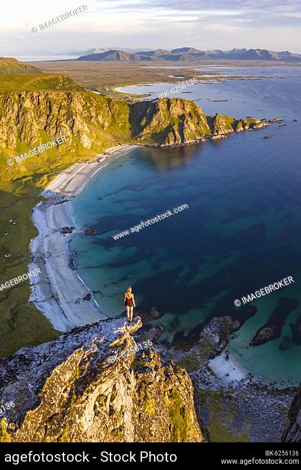Evening atmosphere, hiker standing on a cliff, view to rocks, beach and sea, top of the mountain Måtinden, near Stave, Nordland, Norway, Europe