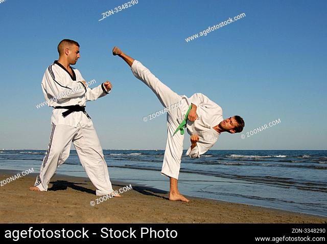 two men are training of taekwondo on the beach