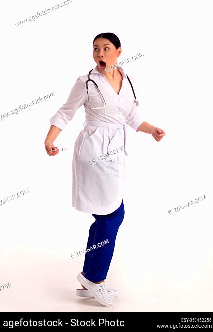 Frightened nurse with syringe on white background. Silly asian doctor pretending to be giving herself injection with syringe and pulling very surprised and...