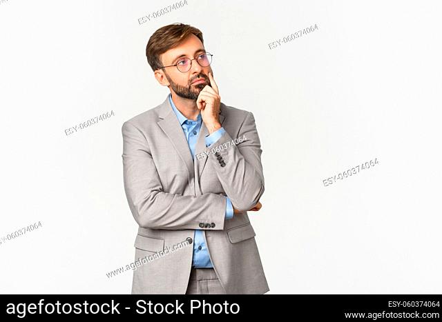 Portrait of thoughtful businessman with beard, wearing grey suit and glasses, thinking about something with serious face, making decision