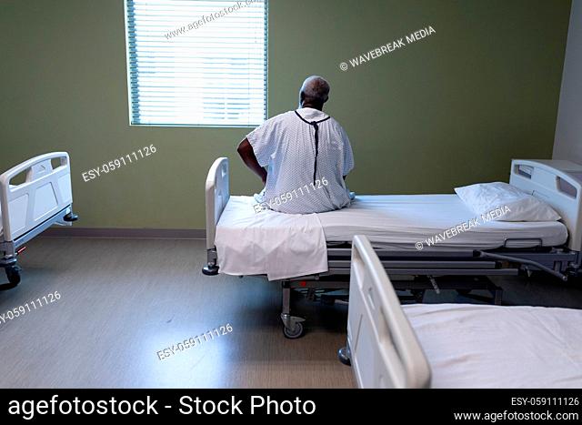 Portrait of african american male patient sitting on hospital bed looking through the window